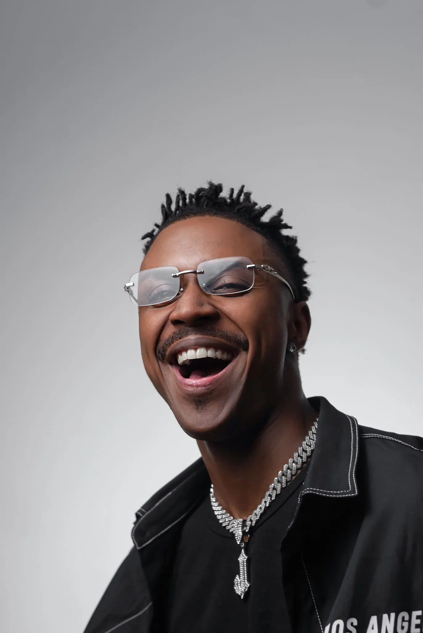 James, cantor de samba e pagode, de óculos e corrente prateada sob luz coral